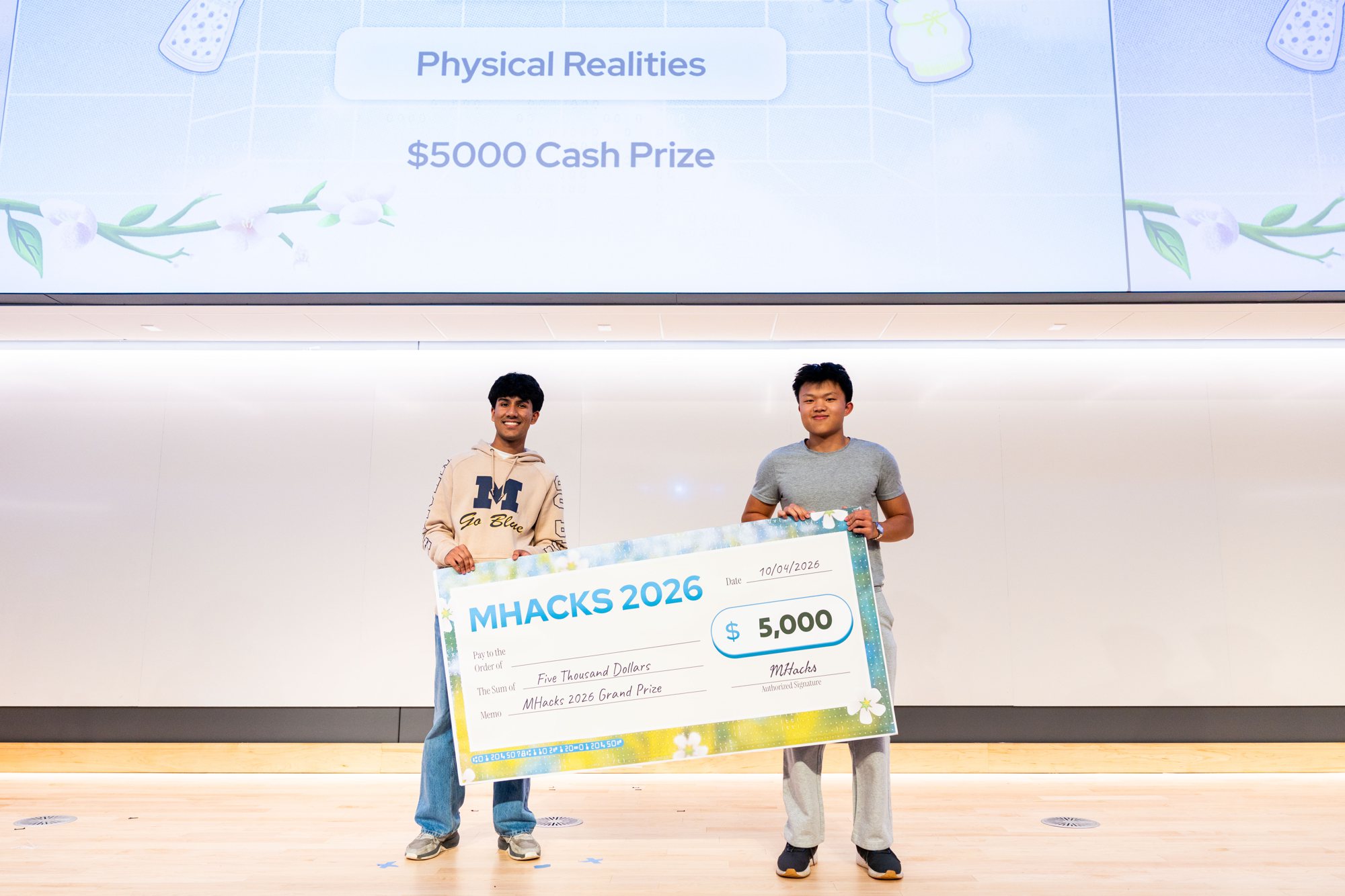 Two winners holding the giant MHacks 2026 $5,000 check on stage