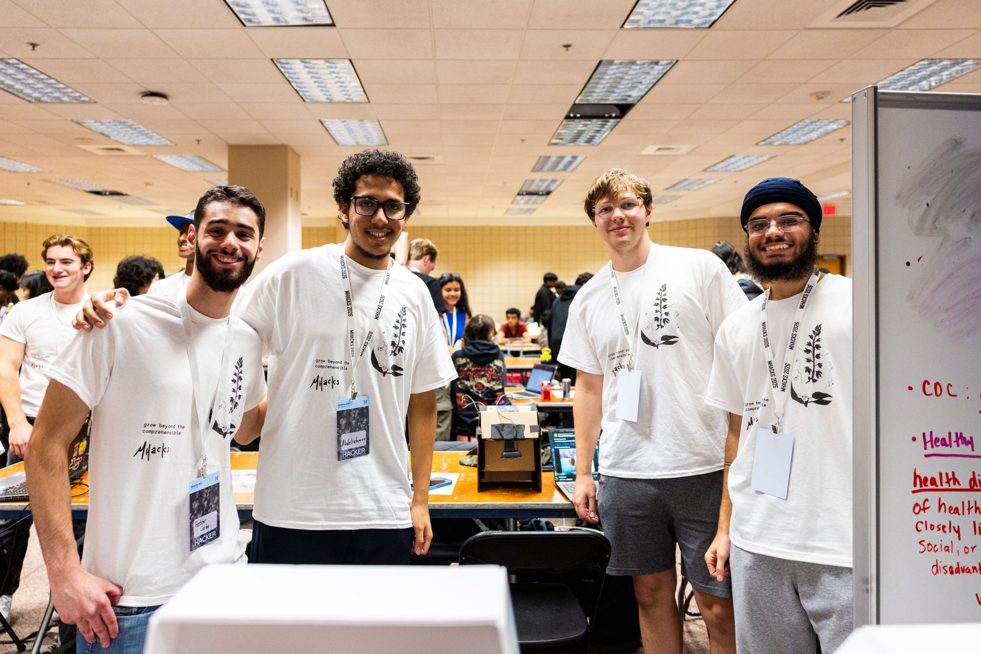 Four hackers wearing the MHacks 2026 t-shirt at their table